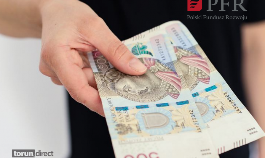 Zdjęcie przedstawia osobę trzymającą dwa banknoty 500 zł i logotyp PFR