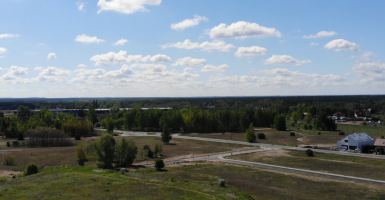 Widok ulicy Przelot i Świdnickiej w Toruniu z lotu ptaka. Asfaltowa droga pośród łąki. Na horyzoncie las i budynki