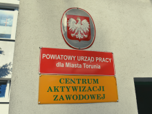Polskie godło i szyldy wiszące przed wejściem do Powiatowego Urzędu Pracy dla Miasta Torunia przy ulicy Mazowieckiej w Toruniu